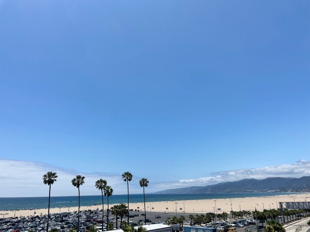 Views of Santa Monica's mountains and beach with palm trees lining a parking lot.