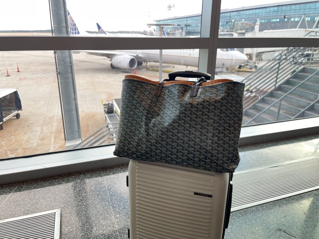 A black carry-on purse on top of a tan luggage at the airport.