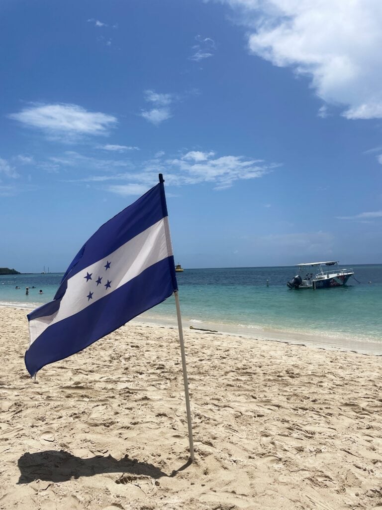 Flag of Honduras waves with West Bay beach in the background. 