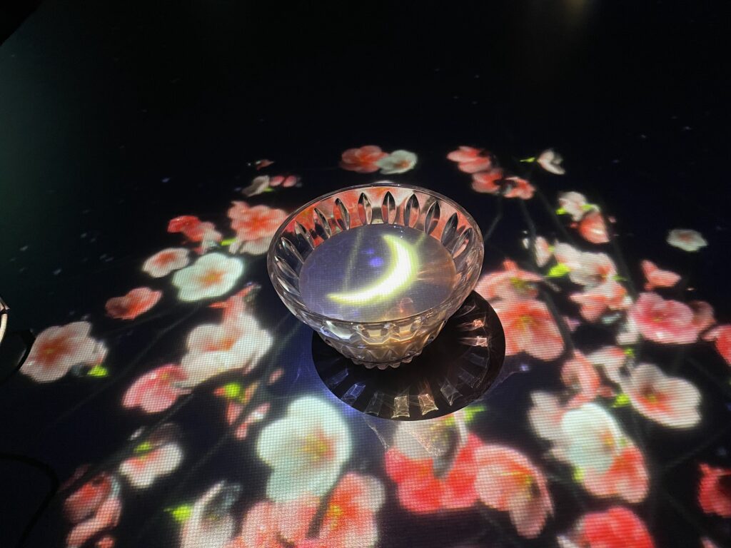 The black golden milk tea on a table with a pink and white digital flower coaster and a moon projected on the drink.