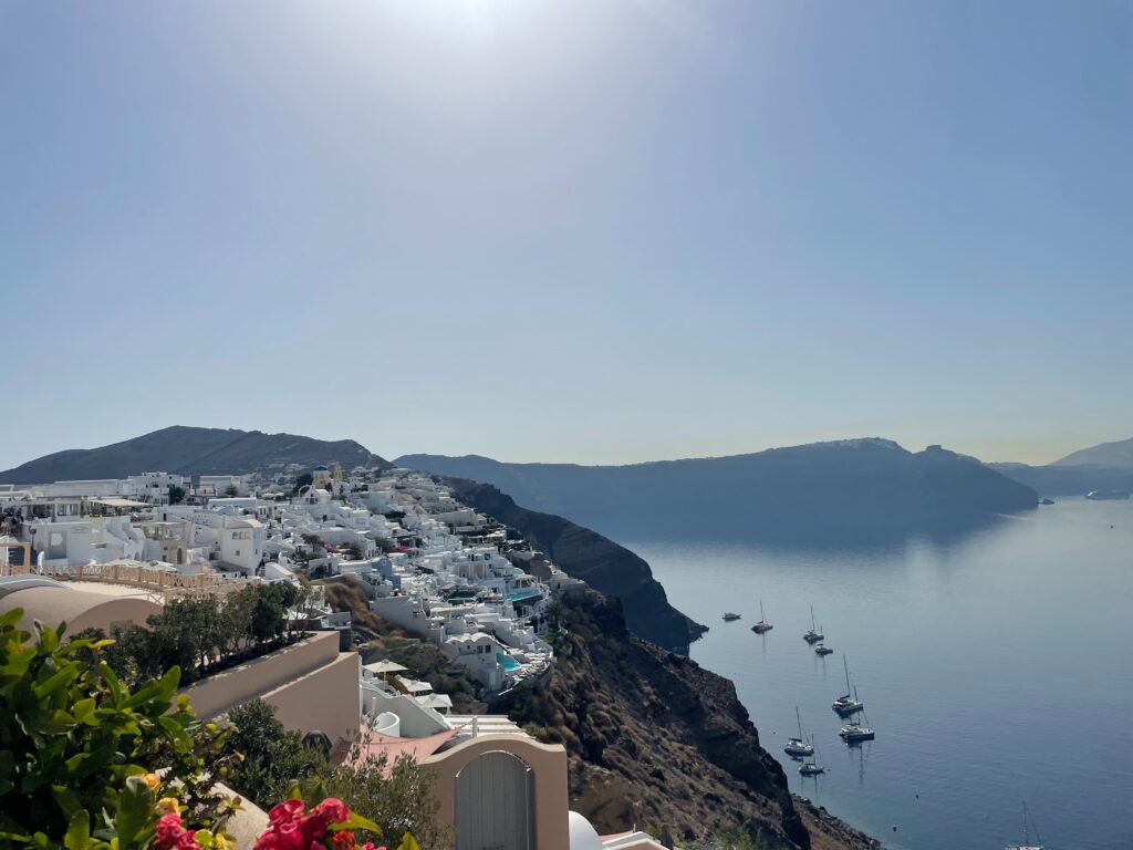 A scenic view of Oia in Satorini, Greece with the sky and ocean meeting while the mountains sit in the background.
