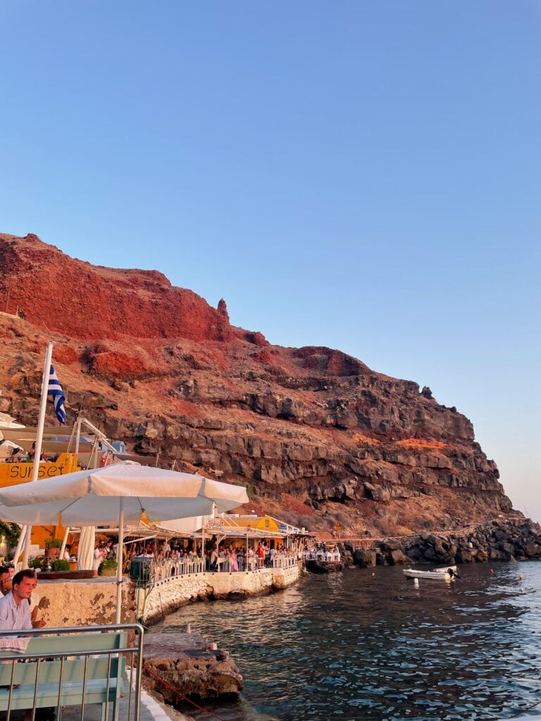 Diners eating at restaurants along Amoudi Bay in Santorini while watching the sun go down.