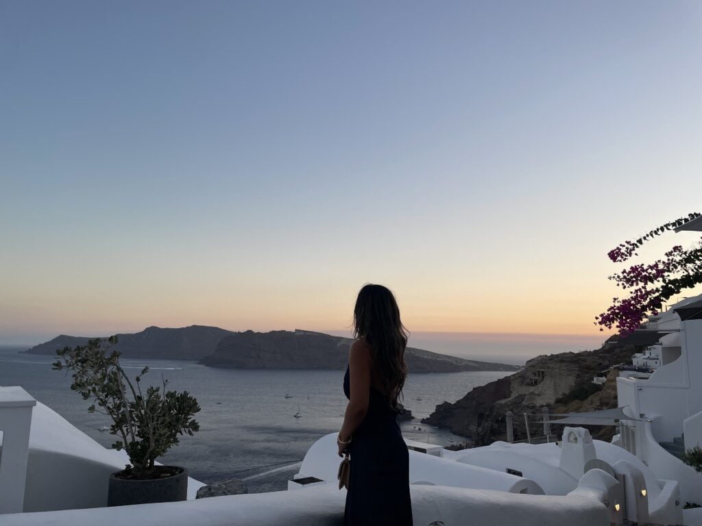 Jenn is taking in the view of Oia as the sun goes down surrounded by white homes and the ocean.